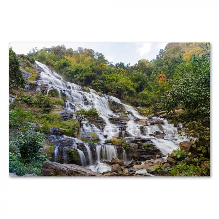 Ein mehrstufiger Wasserfall ergießt sich tosend über Felsen inmitten eines grünen Waldes.